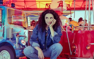Eine junge Frau steht neben einem Jahrmarkt-Ringelspiel für Kinder