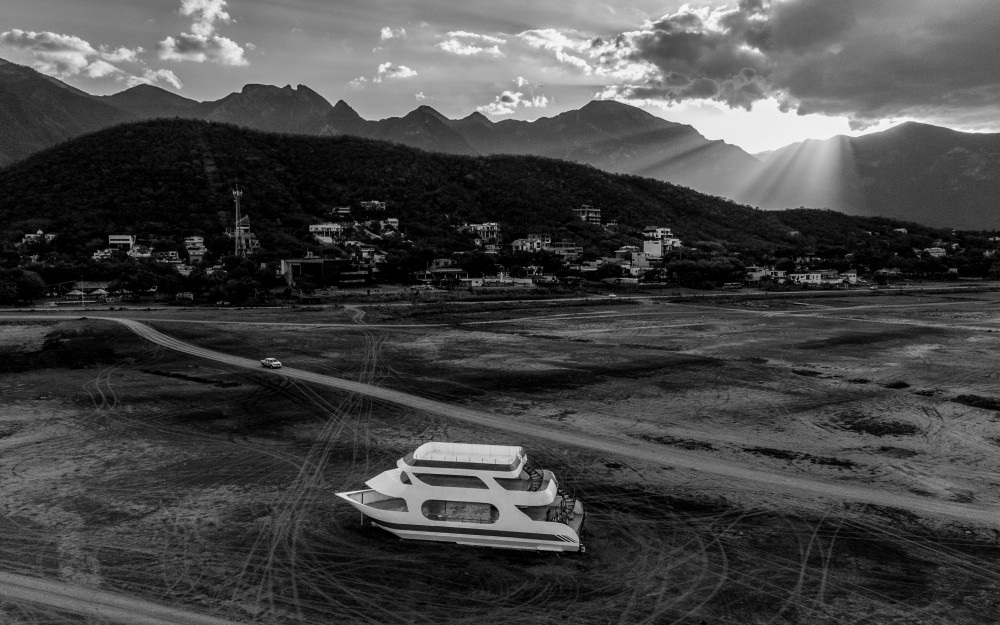 Das Bild zeigt eine s/w Fotografie von César Rodríguez. Zu sehen ist im Vordergrund ein Boot, das in einem ausgetrockneten
                                                Flussbett liegt.